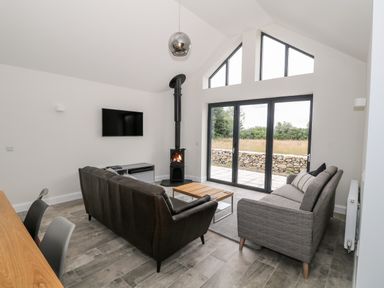 A living room with two sofas a wood stove and large glass doors at Pen Y Cefn