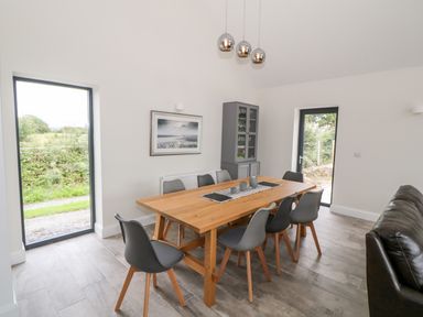 A dining area with a wooden table surrounded by gray chairs and a glass-front cabinet at Pen Y Cefn in Pen Y Cefn