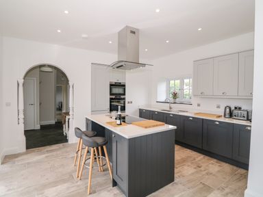 A kitchen with an island and bar stools under a range hood at Pen Y Cefn in Pen Y Cefn