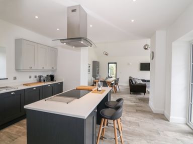 A kitchen with island and stools leading to dining area and living room at Pen Y Cefn in Pen Y Cefn