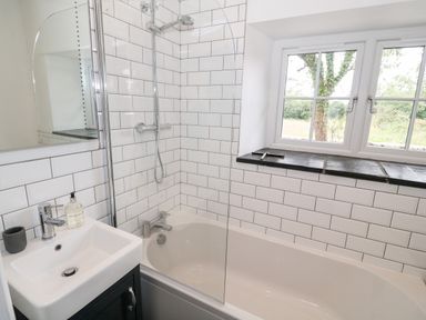 A bathroom with a bathtub shower combination and a sink under a window at Pen Y Cefn