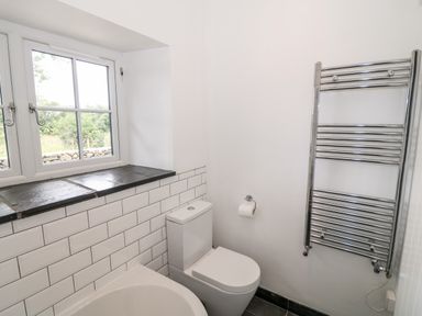 A bathroom with a white toilet a chrome towel radiator a window with stone sill and white tiled walls at Pen Y Cefn in Pen Y Cefn