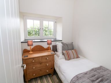 A small bedroom with a single bed next to a wooden chest of drawers and two table lamps at Pen Y Cefn in Pen Y Cefn