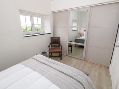 A bedroom with a bed a wooden chair a window and sliding wardrobe doors with a mirror at Pen Y Cefn in Pen Y Cefn