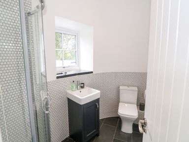 A bathroom with a shower, a sink with a black cabinet, a toilet, and a window at Pen Y Cefn in Pen Y Cefn