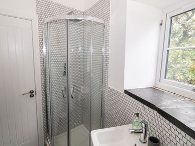 A bathroom with a corner glass shower enclosure a white sink a soap dispenser and a window at Pen Y Cefn