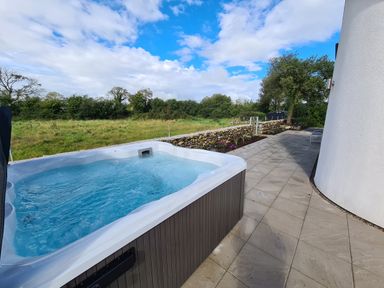 An outdoor hot tub next to a tiled patio with stone wall and grass field beyond at Pen Y Cefn in Pen Y Cefn