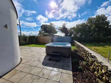 An outdoor patio with a hot tub surrounded by a stone wall and lawn at Pen Y Cefn in Pen Y Cefn