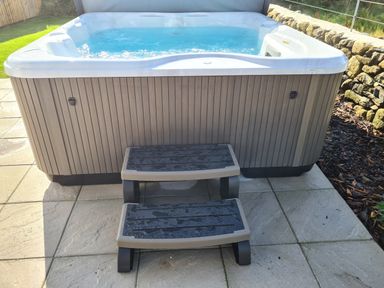An outdoor hot tub with water inside and two plastic steps on a tiled patio at Pen Y Cefn