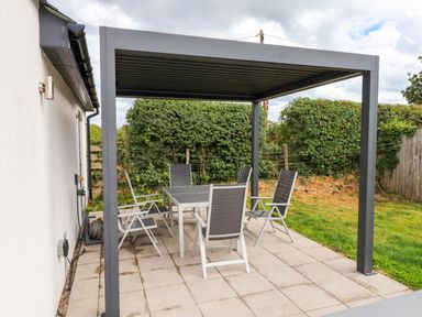 A patio with a table and chairs under a pergola at Pen Y Cefn