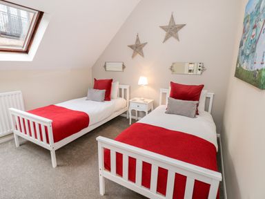 A bedroom with two twin beds with red blankets and pillows a small white nightstand with a lamp star-shaped wall decorations and a skylight window at Valentines Cottage in Stratford-Upon-Avon