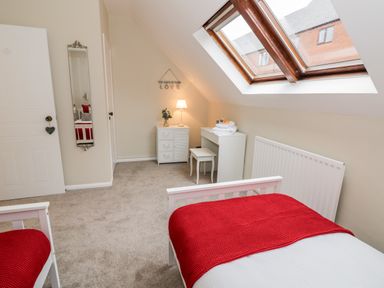 A bedroom with two beds red blankets a desk a mirror and a skylight window at Valentines Cottage Stratford-Upon-Avon