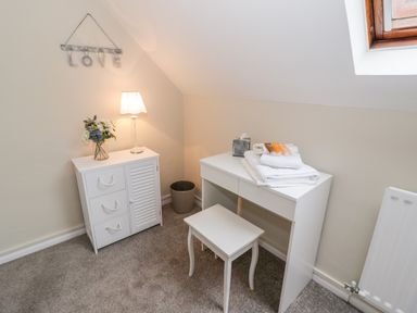 A white dressing table with towels and toiletries next to a small cabinet with a lamp and flowers in a room at Valentines Cottage in Stratford-Upon-Avon