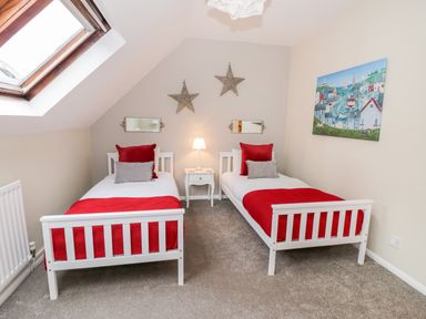 A bedroom with two single beds with red blankets and pillows a small white nightstand with a lamp and a skylight window at Valentines Cottage Stratford-Upon-Avon