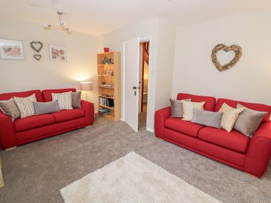 A living room with two red sofas and a wooden bookshelf with decorative items at Valentines Cottage in Stratford-Upon-Avon