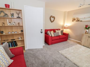 A living room with red sofas a wooden bookshelf a lamp a rug and wall decorations at Valentines Cottage Stratford-Upon-Avon