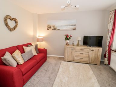 A living room with a red sofa pillows a wooden cabinet a television and decorative items at Valentines Cottage Stratford-Upon-Avon
