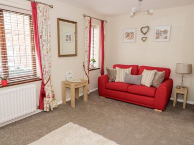 A living room with a red sofa and floral curtains at Valentines Cottage in Stratford-Upon-Avon