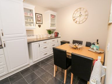 A kitchen with white cabinets a wooden dining table with black chairs and a large wall clock at Valentines Cottage in Stratford-Upon-Avon