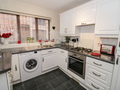 A kitchen with white cabinets a washing machine a gas stove a toaster and a window with blinds at Valentines Cottage in Stratford-Upon-Avon