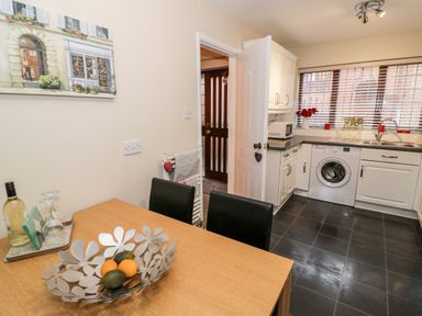 A kitchen with a wooden dining table and black chairs a washing machine under the counter and a window with blinds at Valentines Cottage in Stratford-Upon-Avon