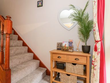 A staircase next to a wooden console table with baskets a plant and decorative items at Valentines Cottage in Stratford-Upon-Avon