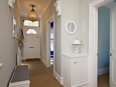 A hallway with a white front door a bench a white cabinet with a lamp and an open doorway at Armorel House in Dartmouth
