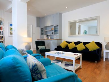 A living room with blue and black sofas yellow cushions a white coffee table and wooden flooring at Armorel House in Dartmouth