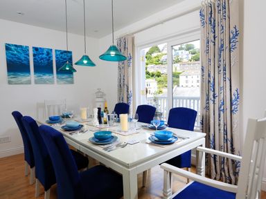A dining room with a white table set with blue dishes and blue chairs by a window with curtains at Armorel House in Dartmouth