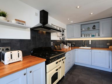 A kitchen with light blue cabinets wooden countertops a black and cream stove a white toaster and kitchen utensils at Armorel House in Dartmouth