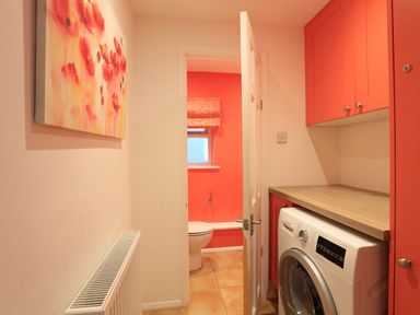 A laundry area with a washing machine and red cabinets next to a small bathroom with a toilet and window at Armorel House in Dartmouth