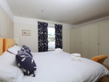 A bedroom with a bed with white linens and blue floral pillows near a window with blue floral curtains and a large wardrobe at Armorel House in Dartmouth