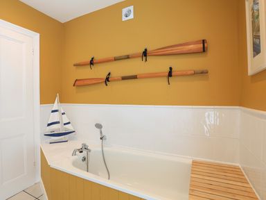 A bathroom with a bathtub a toy sailboat mounted oars and a framed picture at Armorel House in Dartmouth