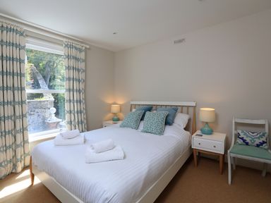 A bedroom with a bed two bedside tables lamps curtains and a chair at Armorel House in Dartmouth