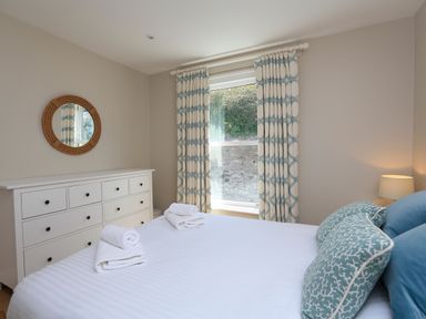 A bedroom with a white dresser a round mirror patterned curtains a bed with towels and pillows at Armorel House in Dartmouth