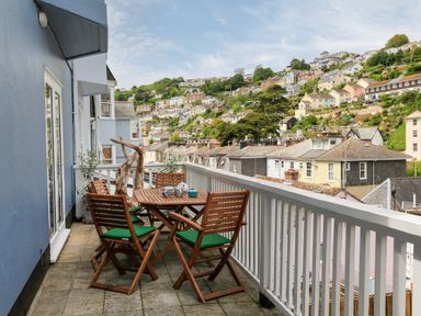 A balcony with a wooden table and four chairs overlooking a hillside with houses at Armorel House in Dartmouth