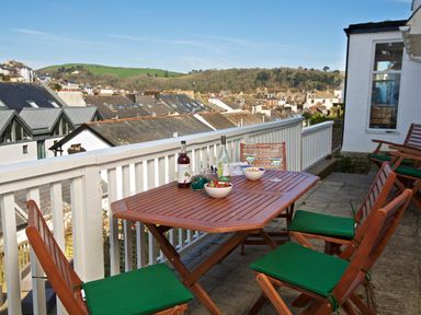 A balcony with wooden table and chairs overlooking rooftops and hills at Armorel House in Dartmouth