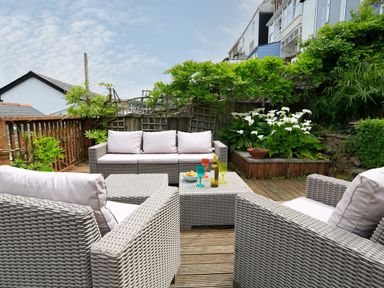 An outdoor seating area with wicker furniture and cushions on a wooden deck with plants and flowers at Armorel House in Dartmouth