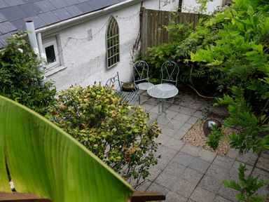 An outdoor patio with metal table and chairs surrounded by plants and a white wall at Armorel House in Dartmouth