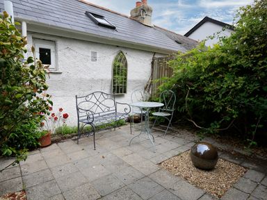 A small patio with metal bench and table set next to a white building with a window and plants surrounding the area at Armorel House in Dartmouth