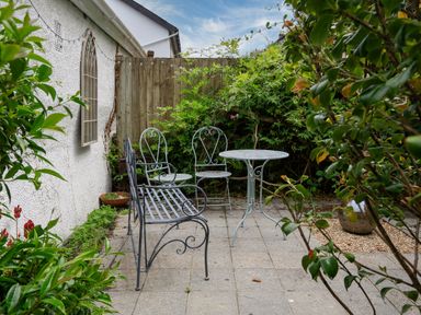 An outdoor patio with metal table and chairs surrounded by plants and a wooden fence at Armorel House Dartmouth