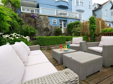 An outdoor patio with wicker furniture and colorful glasses in a garden at Armorel House in Dartmouth
