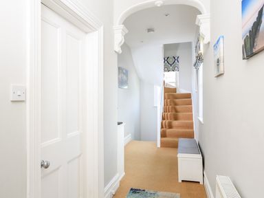 A hallway with a carpeted staircase a white door a small bench with a cushion and wall art at Armorel House in Dartmouth