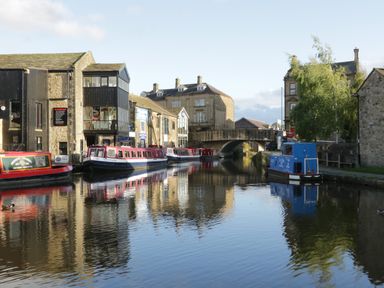 A canal with several narrowboats moored next to stone buildings and a stone bridge over the water at Otter Lodge in Gargrave