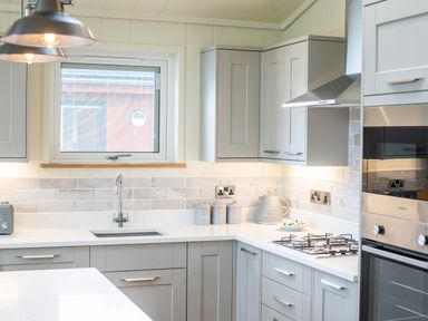 A kitchen with grey cabinets a window a gas stove and countertop appliances at Otter Lodge in Gargrave