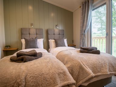 A bedroom with two single beds with gray headboards and folded towels at Otter Lodge in Gargrave