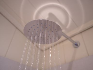 A showerhead with water flowing in a tiled shower at Otter Lodge in Gargrave