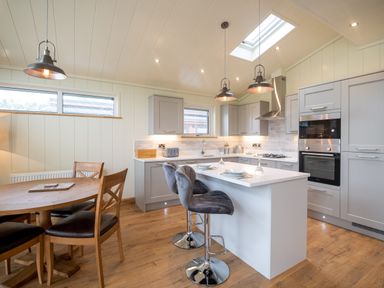 A kitchen with a dining table and two bar stools at Otter Lodge in Gargrave