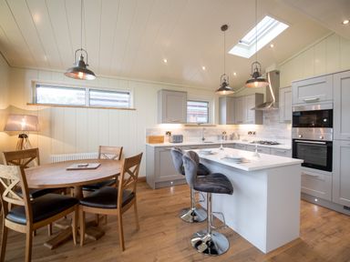 A kitchen with a wooden dining table and chairs and a white island with bar stools at Otter Lodge in Gargrave