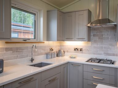 A kitchen with grey cabinets a sink a gas stove and containers on the countertop at Otter Lodge in Gargrave